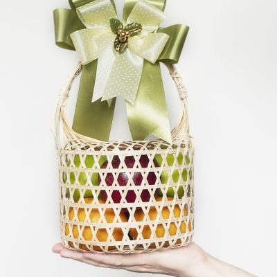 Hand showing fresh fruit souvenir in weaved bamboo package over white gray background - fresh fruit gift set for special occasion concept